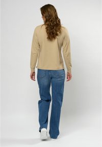 Beige top met lange mouwen en ronde hals, gecombineerd met lichtblauwe wijde jeans. De outfit heeft een gladde textuur en minimale details.