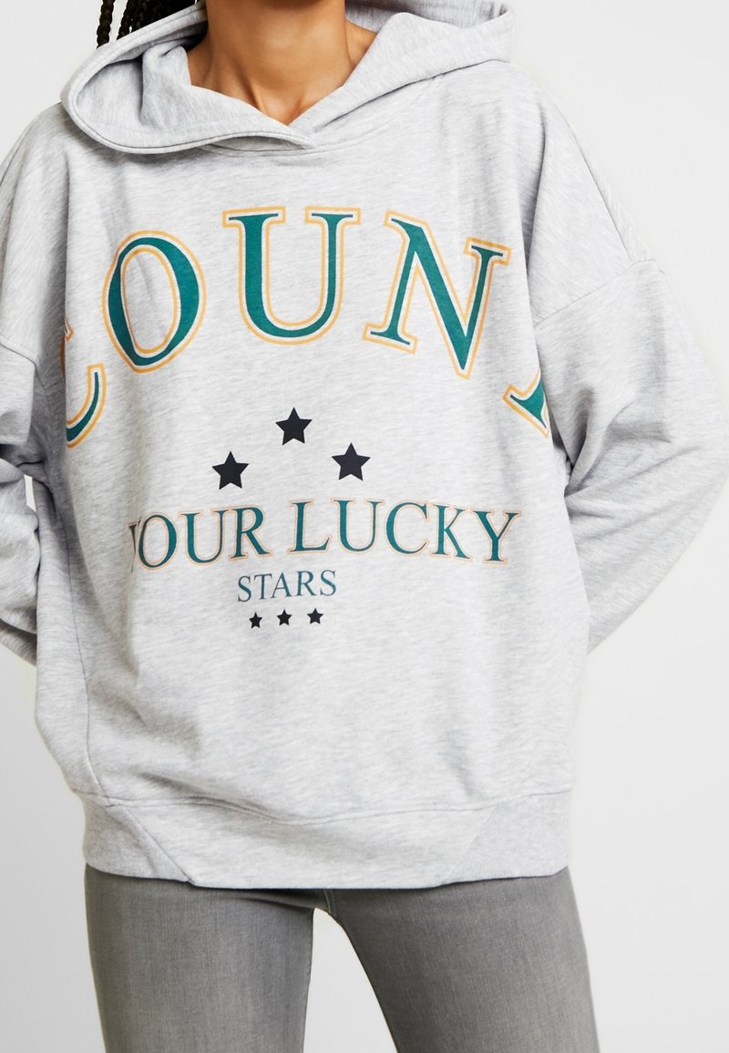 Grå hoodie med en stor tryckt design som visar orden "RÄKNA DINA LYCKOSTJÄRNOR" i teal och orange, med svarta stjärndetaljer.