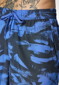 Costumi da bagno blu e neri con motivo a fantasia, dotati di vita elastica e cordoncino, caratterizzati da design a pennellate e una texture liscia.