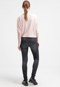 Ljusrosa långärmad topp med uppvikta ärmar, tillsammans med svarta skinny jeans. Jeansen har en urtvättad textur och bakfickor. Svarta skor fulländar looken.