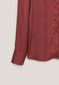 Bordeaux satin skjorte med en glat tekstur, knaplukning foran, lange ærmer og en buet kant. Knapperne matcher stoffarven.