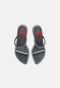 Sandálias de ganga com sola plana, bico aberto e duas tiras adornadas com strass. Apresenta um arco circular e detalhe de logotipo em vermelho contrastante.