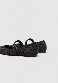 Zapatos planos de estampado de leopardo hechos de tejido suave, con puntera redondeada, correa ajustable con un hebilla circular dorada y tacón bajo.