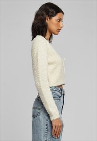 Pulover izrezan u off-white boji, mekane teksture, dugih rukava, s detaljem kravate sprijeda. Uparen s svijetlosmeškim trapericama visokog struka.