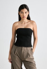 Μαύρη τζιν αμάνικη μπλούζα με εφαρμοστό σχέδιο, με ορατές ραφές και ίσια λαιμόκοψη. Συνδυασμένη με χαλαρές, μπεζ παντελόνες.