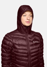 Giacca isolata color marrone con design a quadri orizzontali e cappuccio aderente. Presenta una zip frontale e un logo nella zona del petto.