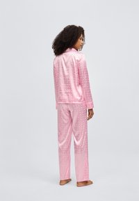 Rosa Satinkleid-Pyjama-Set mit einem strukturierten Blumenmuster, langen Ärmeln und locker sitzender Hose, mit sichtbarem Markenlogo auf der Rückseite.