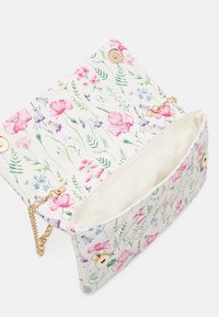 Kabelka s květinovým vzorem na bílém pozadí, zlaté kovové detaily a řetízkový popruh. Otevřená, odhalující krémovou podšívku.