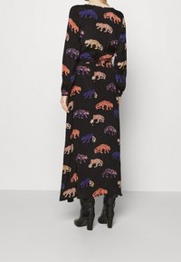Maxiklänning i svart tyg med färgglada björn-mönster i orange, lila och blått. Långa ärmar och midja med dragsko.