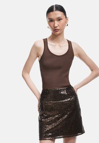 Bruine geribbelde tanktop gecombineerd met een glanzende zwarte pailletten mini rok. De tanktop heeft brede bandjes en een ronde halslijn, wat de silhouet accentueert.