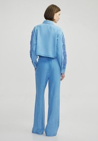 Chaqueta de mezclilla azul clara con mangas de encaje, combinada con jeans de pierna ancha de cintura alta a juego. Textura suave, diseño casual.