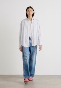 Hvit og blåstripet skjorte med knapper, kombinert med høytlivs lys blå jeans og rosa joggesko, stående mot en nøytral bakgrunn.