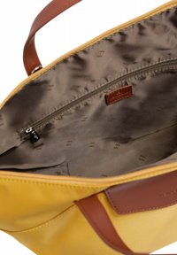Geel handtas met bruin leren handvatten. Het interieur heeft een gladde, bruine voering met een ritszak en een subtiel reliëfpatroon.