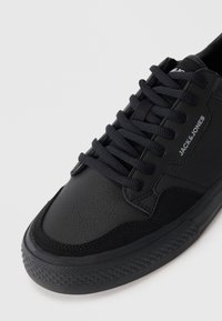 Black sneaker featuring textured synthetic upper, smooth accents, durable rubber sole, and padded tongue with flat laces.