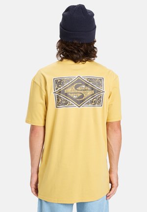 Gelbes Baumwoll-T-Shirt mit kurzen Ärmeln, das auf der Rückseite ein grafisches Design in Schwarz und Weiß aufweist und einen lockeren Schnitt hat.