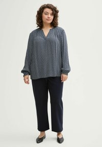 Blusa de estampado navy con escote en V y mangas largas, combinada con pantalones oscuros y zapatos planos. Tejido suave, corte relajado.
