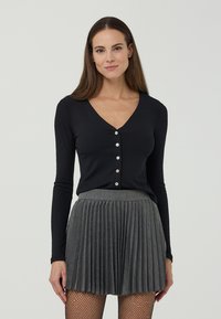 Top nero a maniche lunghe con scollo a V e cinque bottoni davanti, abbinato a una gonna grigia plissettata. Tessuto lavorato a maglia con una texture liscia.