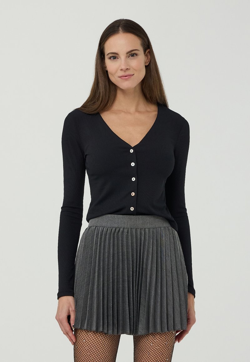 Top nero a maniche lunghe con scollo a V e cinque bottoni davanti, abbinato a una gonna grigia plissettata. Tessuto lavorato a maglia con una texture liscia.