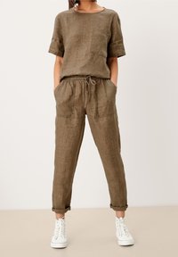 Linnen twee-delige outfit in aardetinten, bestaande uit een korte mouw top met een zak en sweatpants met een trekkoord en opgerolde manchetten, gecombineerd met witte sneakers.
