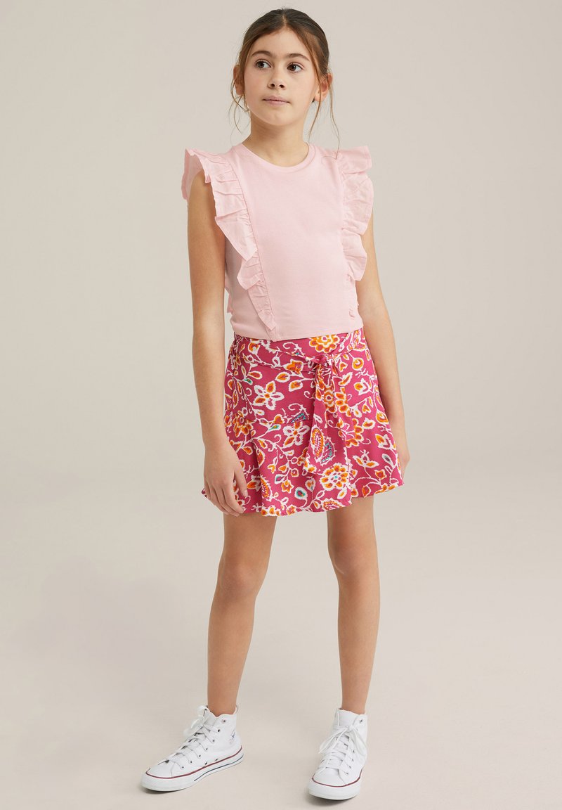 Rosa volangstopp med en blommönstrad rosa kjol som har orange och gula accenter, tillsammans med vita högskurna sneakers.