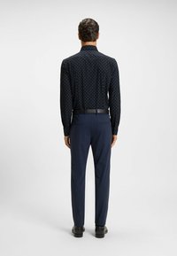 Marineblauw overhemd met lange mouwen en witte stippen, met een geknoopt kraag, gecombineerd met donkerblauwe broek en zwarte schoenen. Riemen zichtbaar op de taille.
