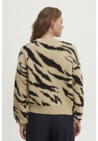 Fuzzy beige trui met zwarte tijgerstrepen, ronde halslijn en geribde manchetten en zoom. Beschikt over een zachte, gestructureerde oppervlakte.