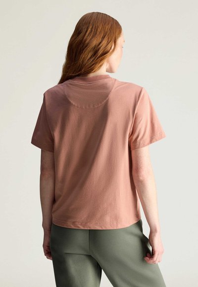 Maglietta a maniche corte, taglio rilassato in cotone rosa chiaro con scollatura rotonda e texture liscia, abbinata a pantaloni verde oliva.