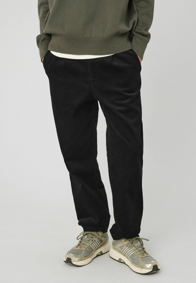 Pantalons en velours côtelé noir à coupe droite, dotés de deux poches latérales et d'un tissu texturé. Associés à des baskets vert-gris.