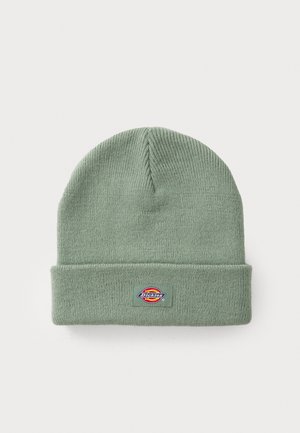 Grønn strikket lue med foldet oppkant, laget av mykt materiale. Har et rektangulært logo-patch i levende farger på forsiden.