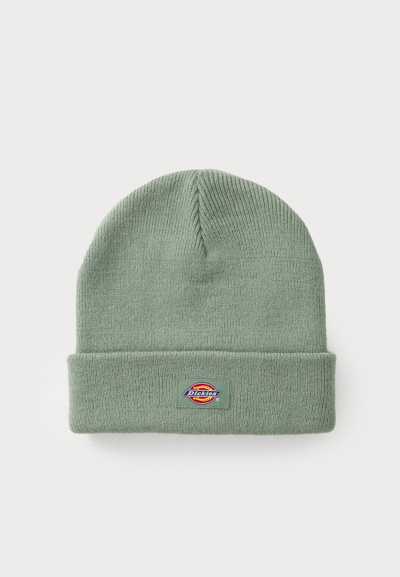Boné de malha verde com uma dobra na bainha, feito de material suave. Apresenta um emblema retangular em cores vibrantes na parte da frente.