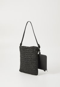Sort vævet taske med en struktureret, rektangulær form. Har en lang rem, en glat sort sidelomme og teksturerede mønstre overalt.