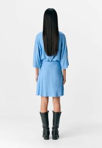 Robe bleue jusqu'aux genoux avec des manches trois-quarts, ornée de broderies délicates. Associée à de grandes bottes noires plates.