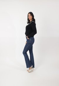 Suéter negro recortado con acentos blancos, combinado con jeans acampanados azules y sandalias de tacón blancas. Tejido suave, diseño ajustado.