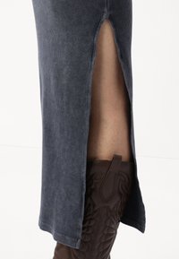 Δερμάτινη φούστα με ραβδωτή υφή, που διαθέτει πλάγιο σκίσιμο και σκούρο μπλε χρώμα, συνδυασμένη με καφέ κεντητές δερμάτινες μπότες.