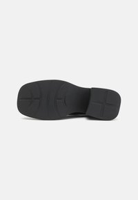 Sola de sapato preta com material de borracha texturizada, apresentando padrões de profundeza e um salto plano. Forma ligeiramente curvada para conforto.