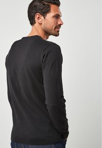 Sorte bomuldsweater med rund hals, ribbede ærmer og kant. Glat tekstur, tætsiddende form og minimalistisk design, iført med blå jeans.