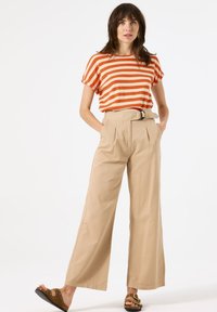 Gestreepte oranje en witte top met korte mouwen, gecombineerd met hoog-wijde beige broek met een riem en platte sandalen.