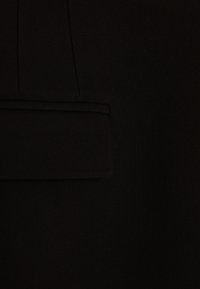 Schwarzer Stoff mit glatter Textur und einer ordentlich genähten Klappentasche. Schlichtes Design ohne sichtbare Muster oder Beschläge.