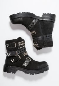 Botas negras hasta el tobillo con múltiples correas decorativas, hebillas y tachuelas. Cuero texturizado y suela de goma con un diseño de taco robusto.
