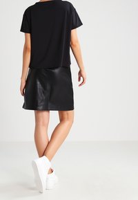 Top negro de manga corta con un corte holgado, combinado con una falda mini de cuero negro. El conjunto se completa con zapatillas blancas.