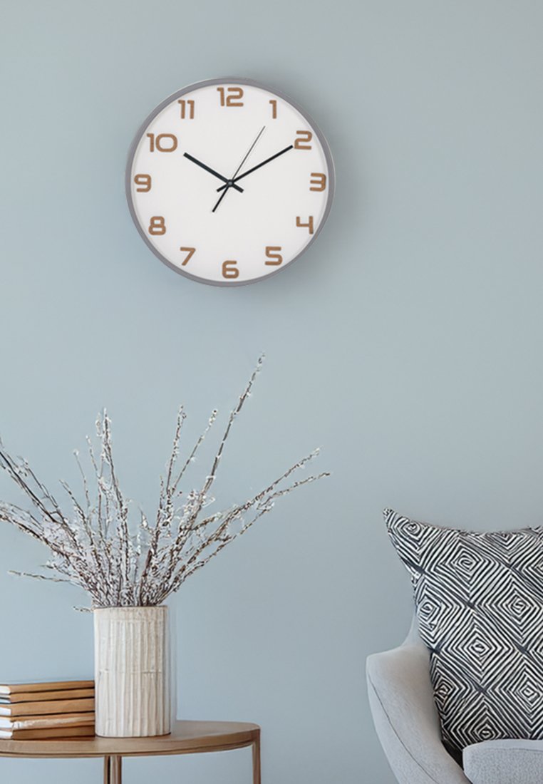 Runde Wanduhr mit weißem Ziffernblatt, braunen Ziffern und schwarzen Zeigern. Holzrahmen, minimalistisches Design, montiert an einer hellblauen Wand.