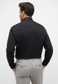 Zwarte langemouwen shirt met een puntige kraag, gecombineerd met lichtgrijze broek met een gladde textuur en achterzakken met knopen.