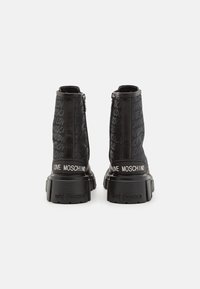 Bottines noires avec un dessus texturé arborant un motif répété « LOVE MOSCHINO » et une semelle épaisse. Détails de fermeture éclair à l'arrière.