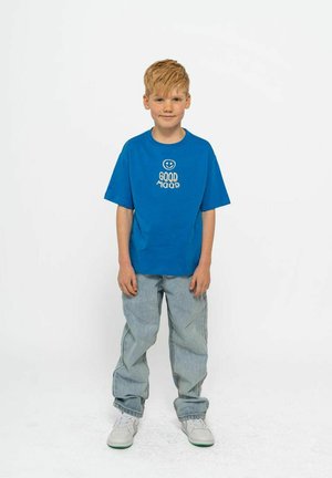 Blauwe katoenen T-shirt met witte tekst "GOOD MOOD" en een smileygraphic, gecombineerd met lichte denim broek en witte sneakers. Eenvoudig, casual ontwerp.