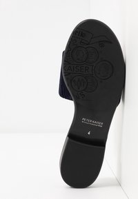 Semelle de chaussure noire avec finition texturée, comprenant des logos et motifs en relief. Talon plat avec de légères rainures pour la traction et l'adhérence.