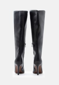 Bottes hautes en cuir noir jusqu'aux genoux avec talons stiletto, dotées d'une finition lisse et de détails zippés à l'arrière. Design classique et forme ajustée.