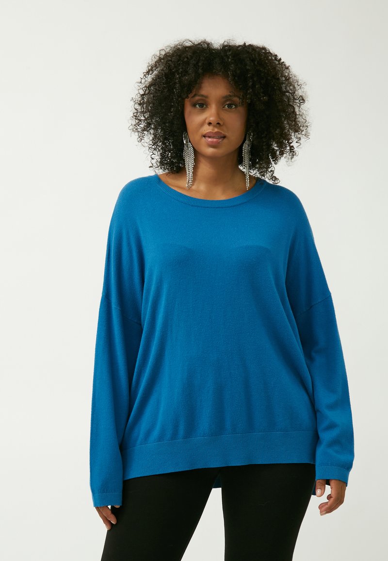 Blaues oversized gestricktes Sweatshirt mit rundem Halsausschnitt und langen, weitem Ärmeln. Weiche Textur, gerippter Saum und eine lässige Passform.