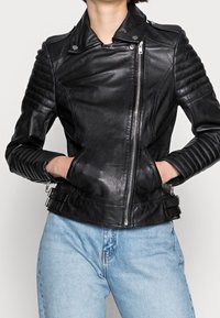 Černá kožená motorkářská bunda s prošívanými detaily na ramenou, asymetrickým zapínáním na zip a bočními kapsami na zip. Hladká textura, přiléhavý střih.
