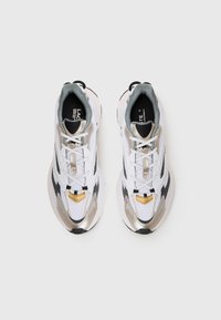 White athletic shoes with silver and black accents, mesh upper, round toe, lace-up closure, and prominent gold detail on the toe cap.