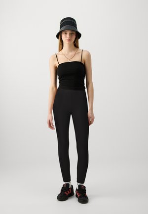 Top aderente nero, leggins neri a vita alta, scarpe da ginnastica nere e rosse e un cappello a secchiello striato nero. Accessori minimi visibili.